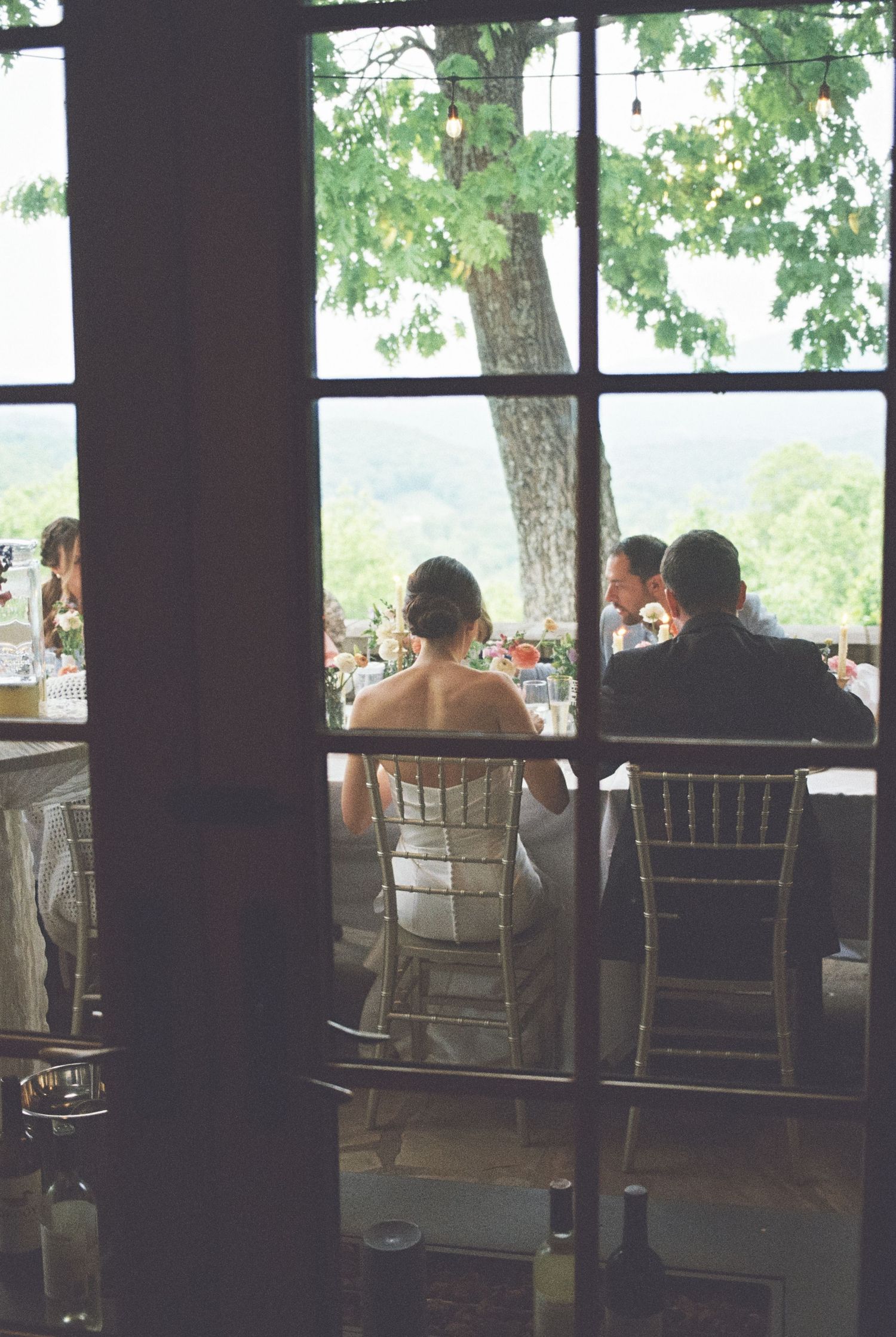 People seated on a covered porch overlooking a scenic outdoor view through dark wooden columns.