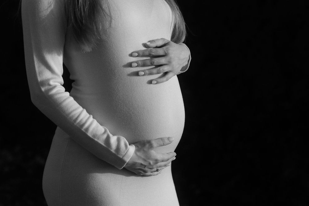 Black and white artistic maternity photo showing hands cradling a pregnant belly while wearing a light sweater in Tenerife.