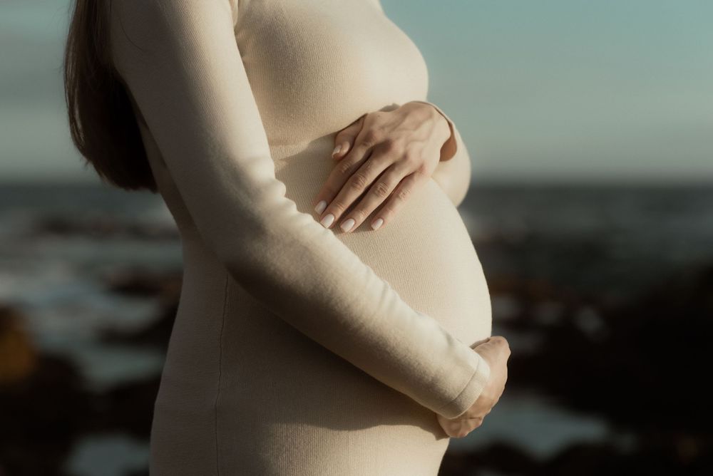 Silhouette of a pregnant woman's belly gently cradled by hands against a soft, blurred background. Pregnancy photoshoot in Tenerife.