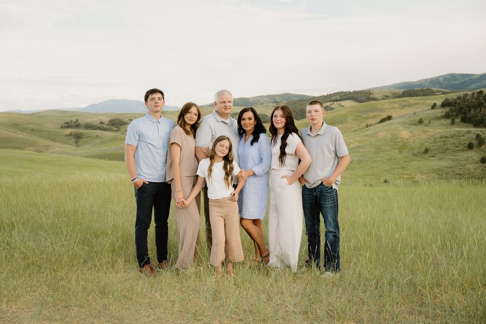 A group in coordinated neutral outfits poses together in a sunlit grassy field during golden hour.