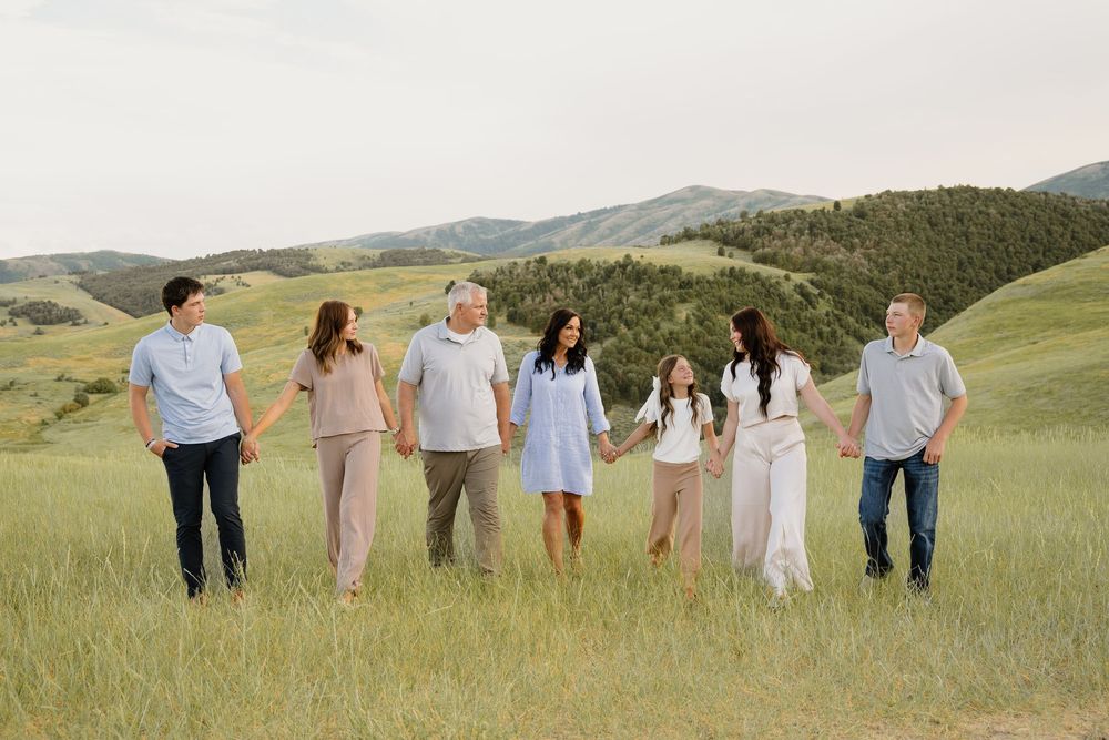 Group of people walking together through a scenic green hillside meadow with rolling mountains in the background.