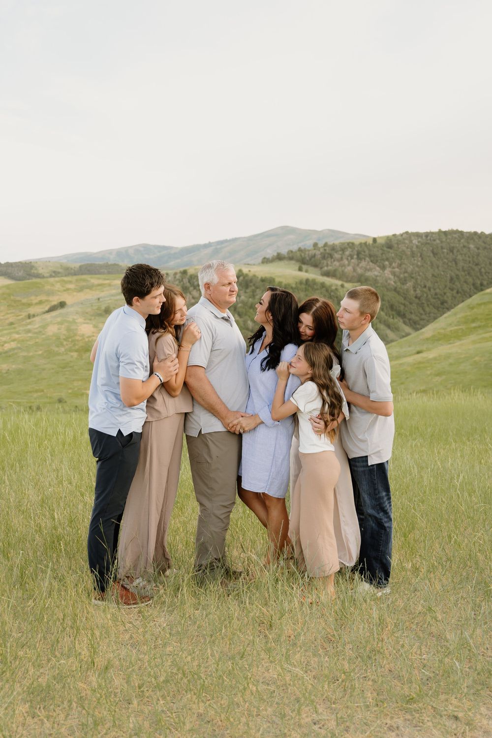 A group poses together in casual attire against a backdrop of rolling green hills and mountains on a sunny day.