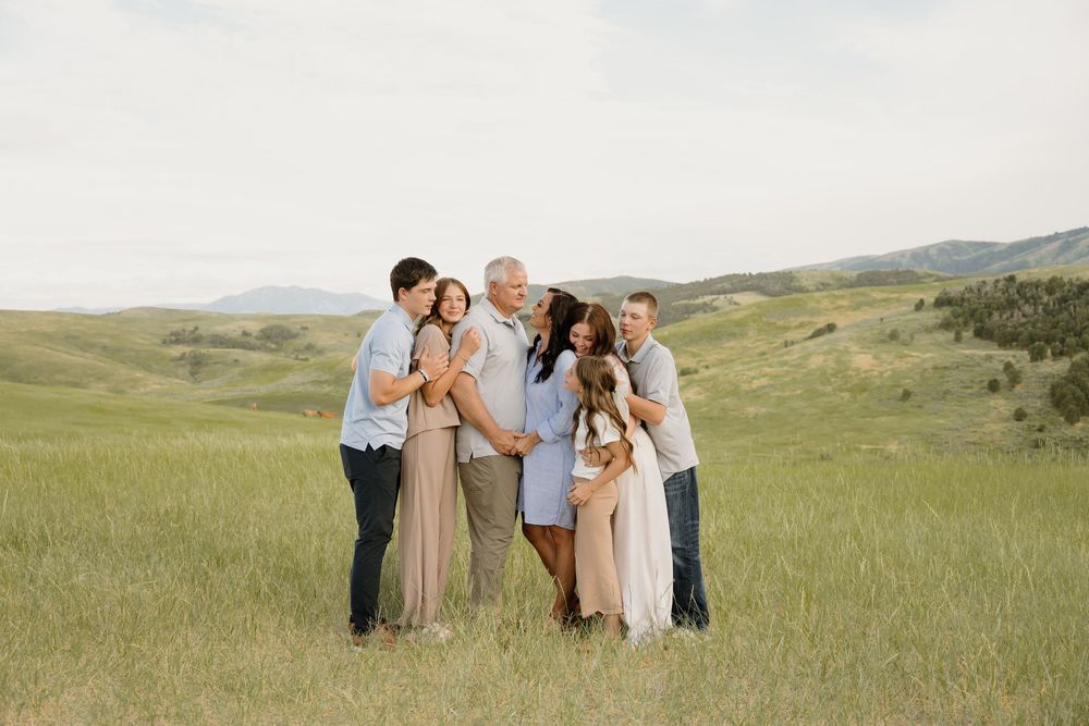 A family poses together in an open grassy meadow with rolling hills and mountains in the background on a sunny day.