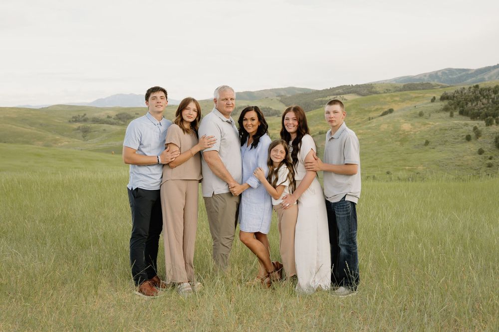 A group of five people stand together in casual attire on a green hillside with rolling mountains in the background.