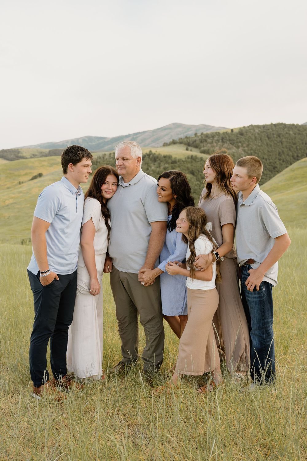 A group poses together in casual attire on a grassy hillside during sunset with mountains in the background.