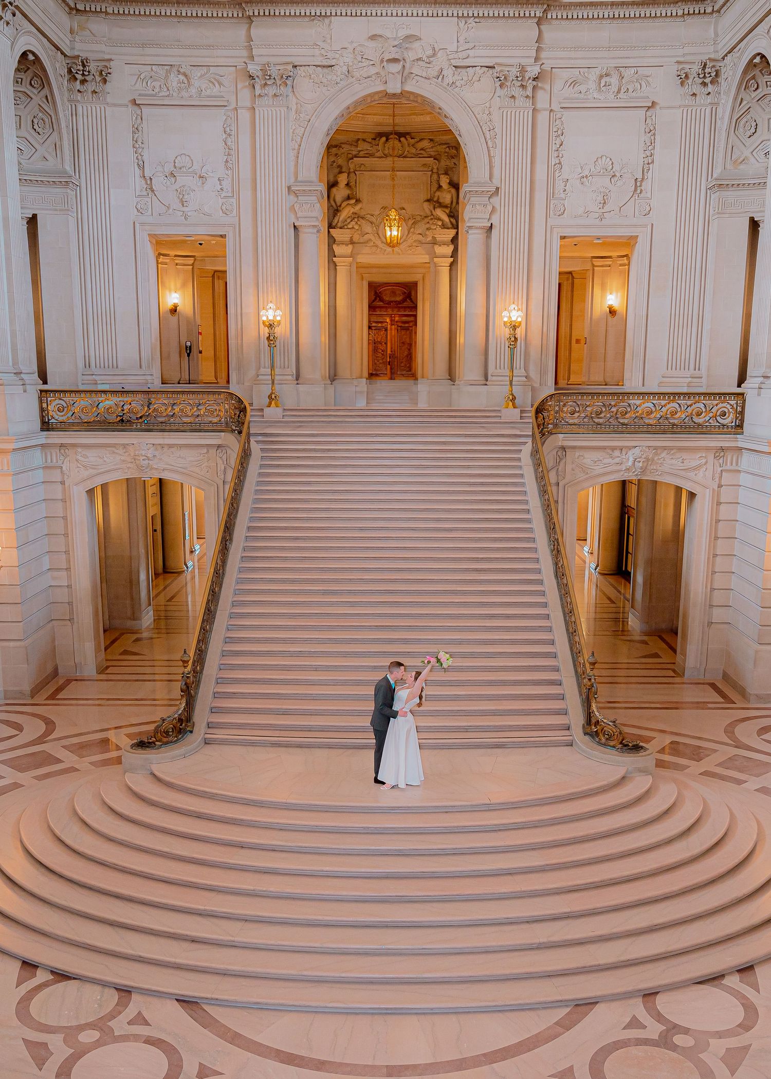 A couple sharing an intimate moment near an ornate stone column in formal wedding attire.