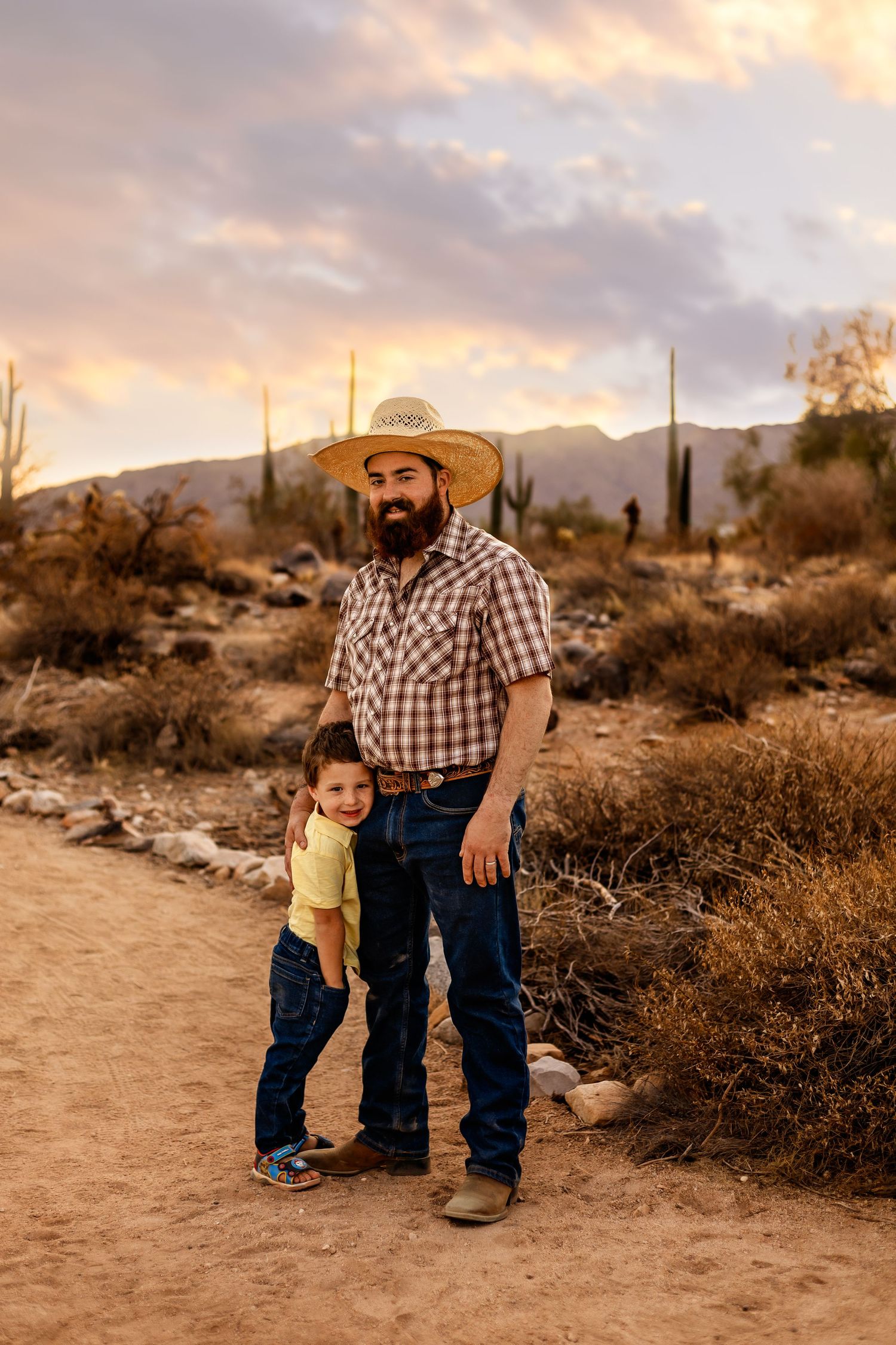 A child and adult share heartwarming moments along a desert trail at sunset with saguaro cacti in the background.