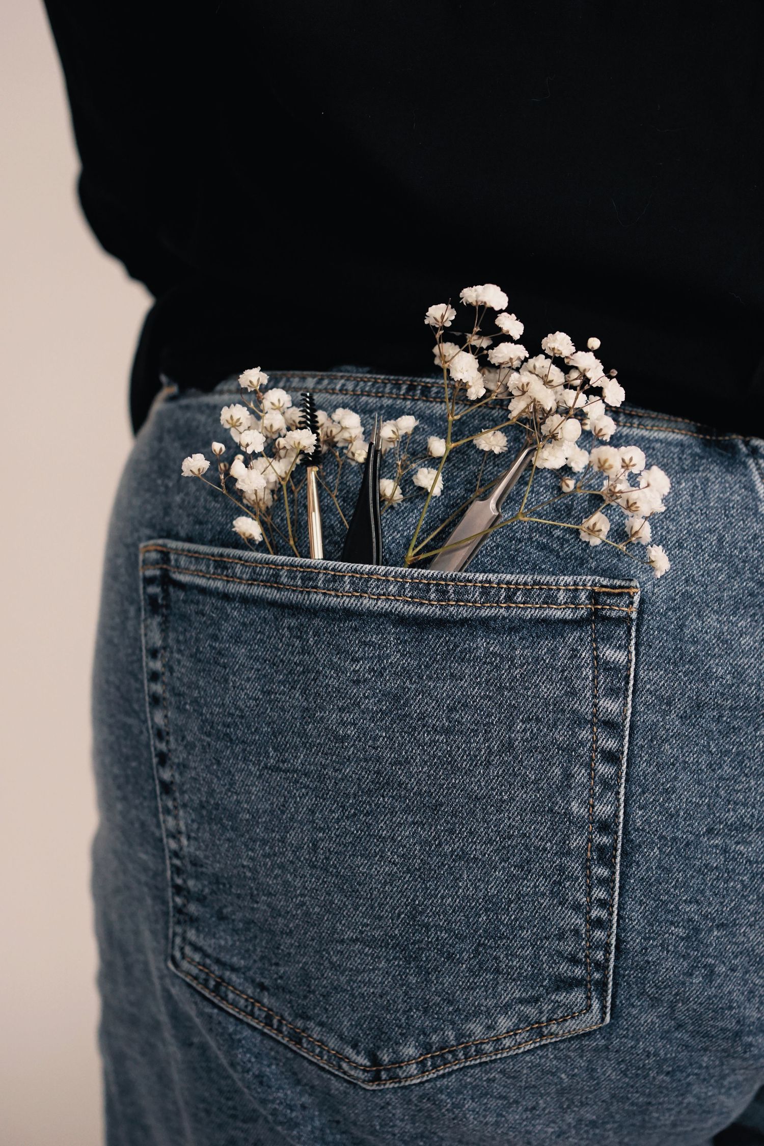 Small white baby's breath flowers tucked into the back pocket of blue denim jeans against a black background.