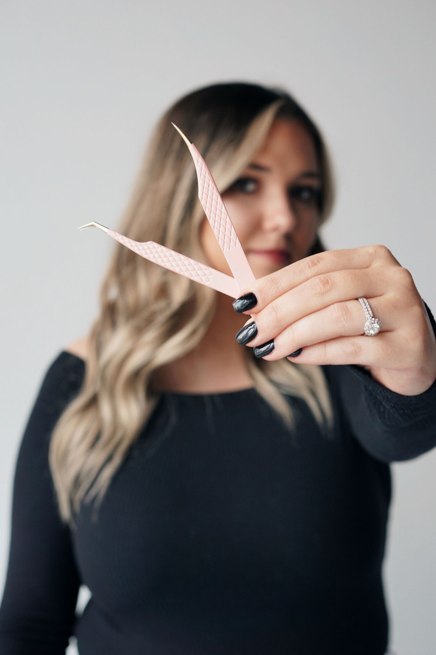 Woman in black long sleeve top holds an origami paper crane while showing off engagement ring with navy blue nails.