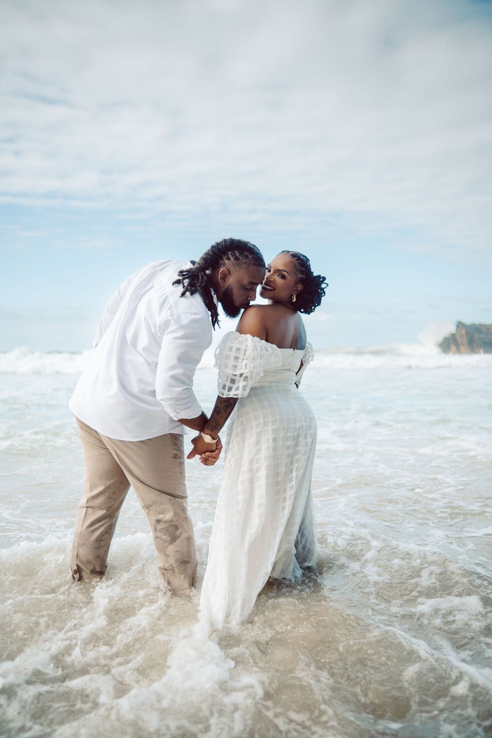 A romantic beach photoshoot sequence captures a couple falling playfully into the ocean waves while wearing white attire.