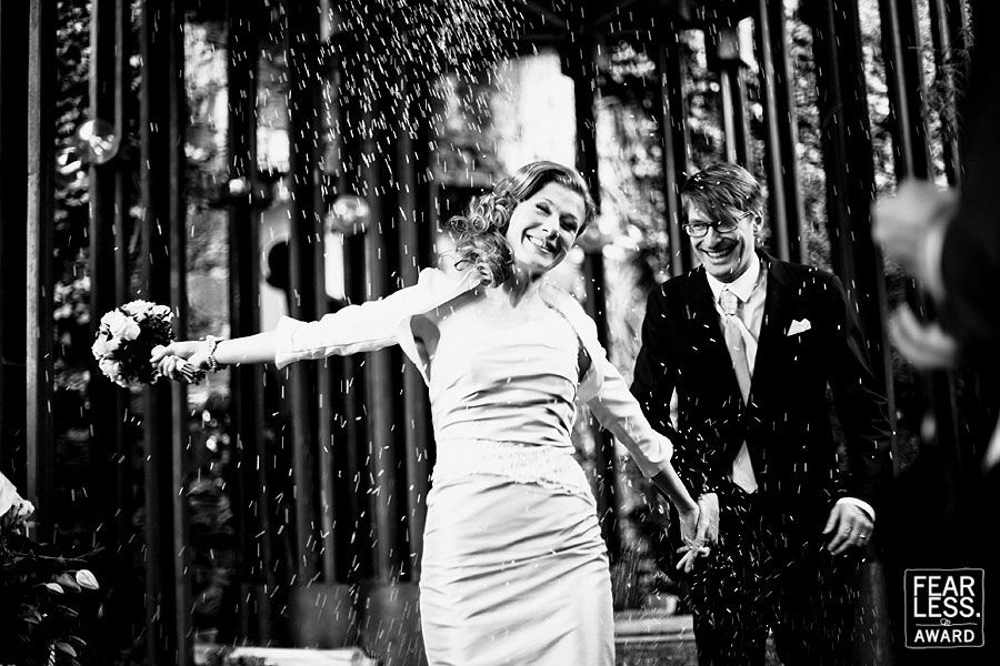 A joyful black and white wedding moment captured in the rain with trees in the background.