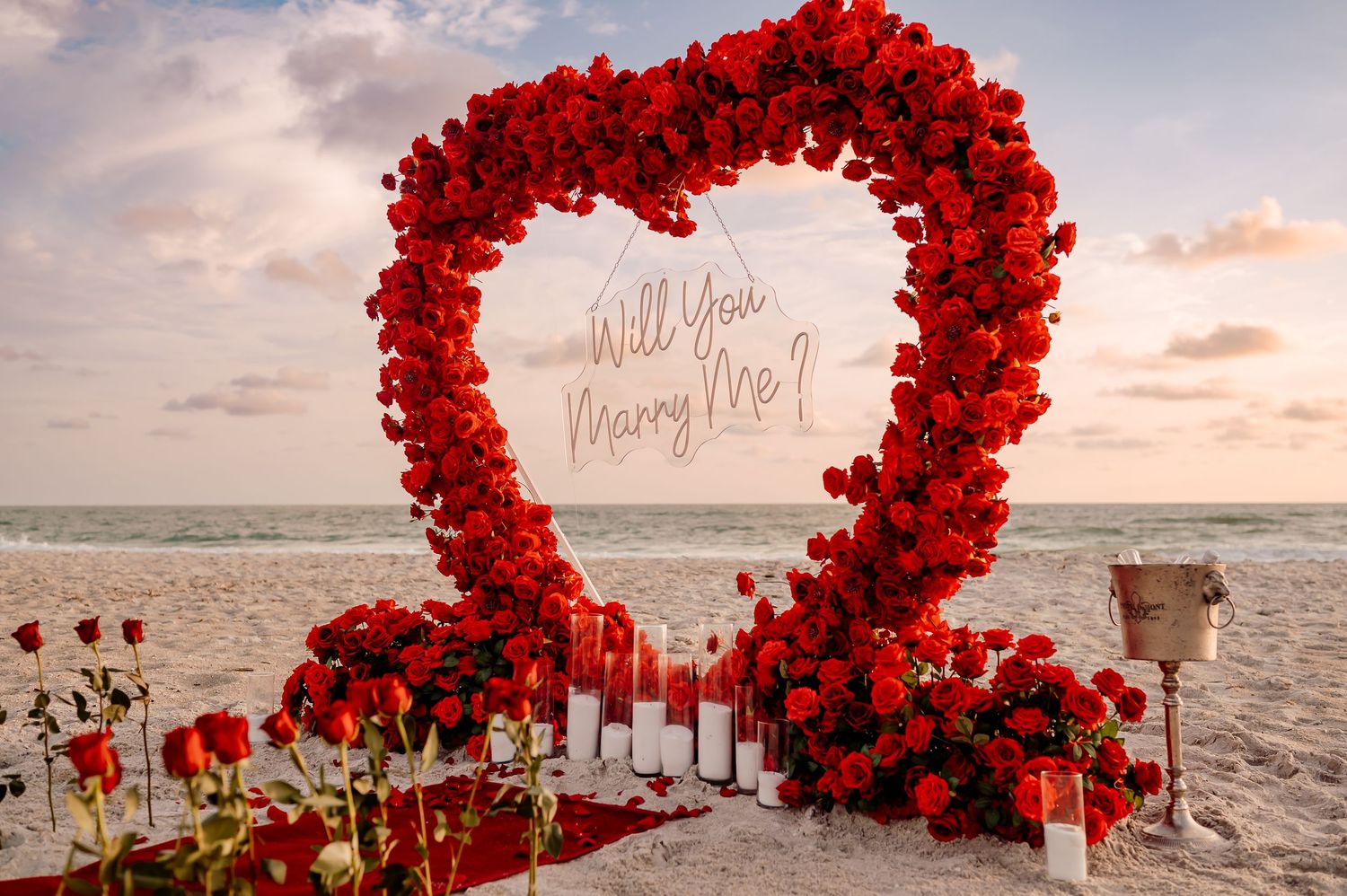 Elegant red rose flower arch on the sand set up for a beach engagement.
