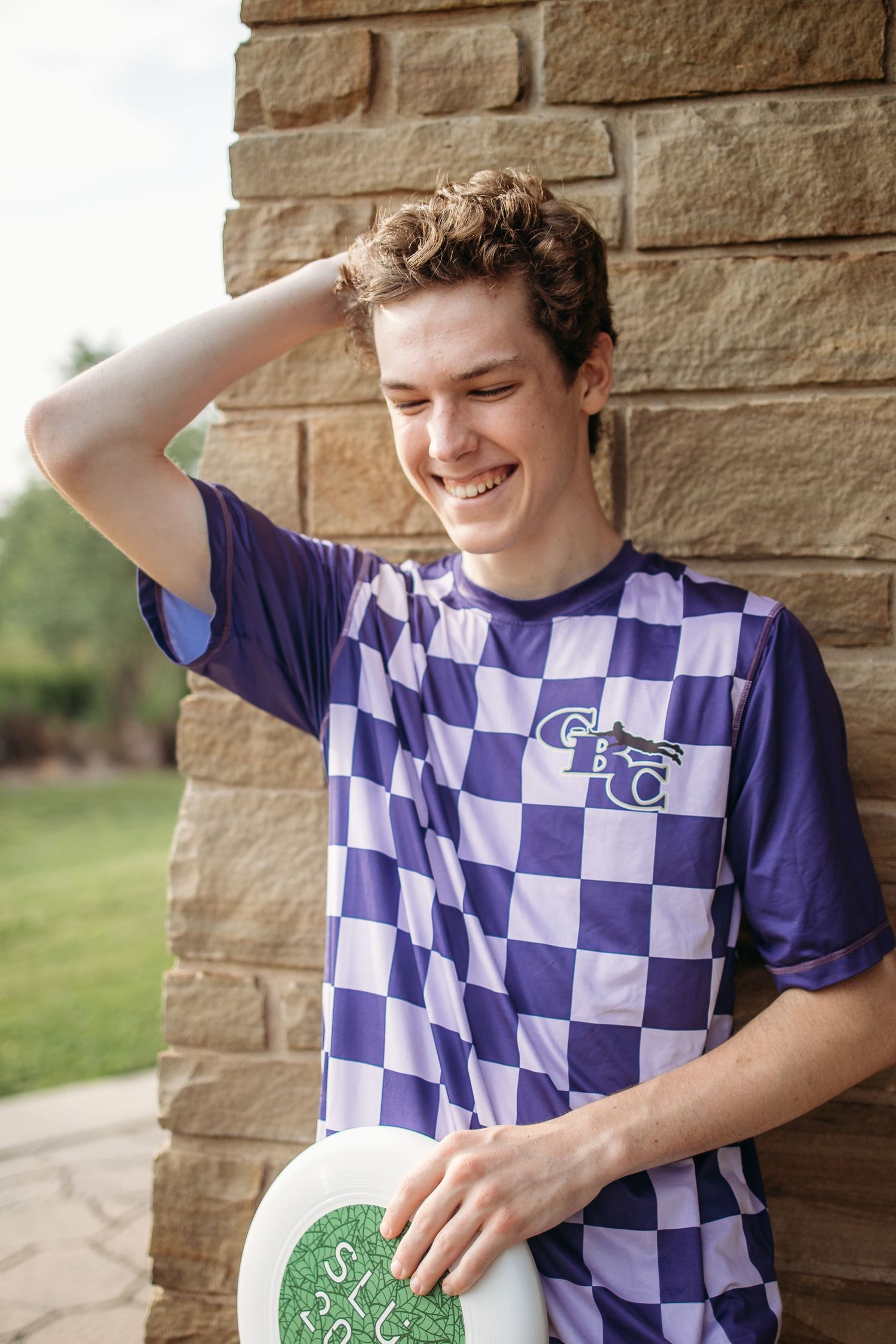A graduating senior in an ultimate jersey poses playfully with a frisbee against a stone wall backdrop during his photoshoot St. Charles, MO