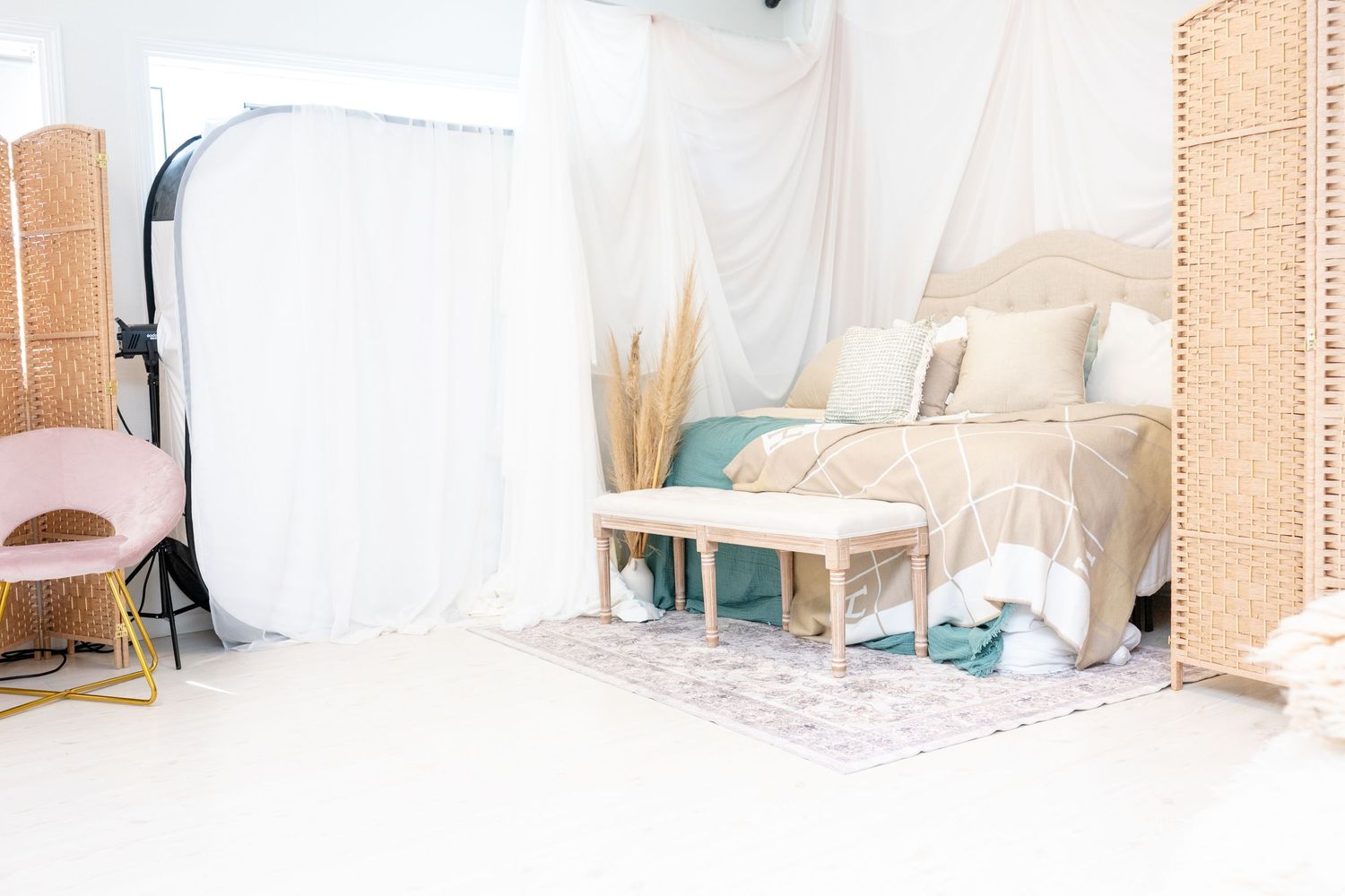 Studio bedroom setup with white curtains, rattan screen and teal accents.