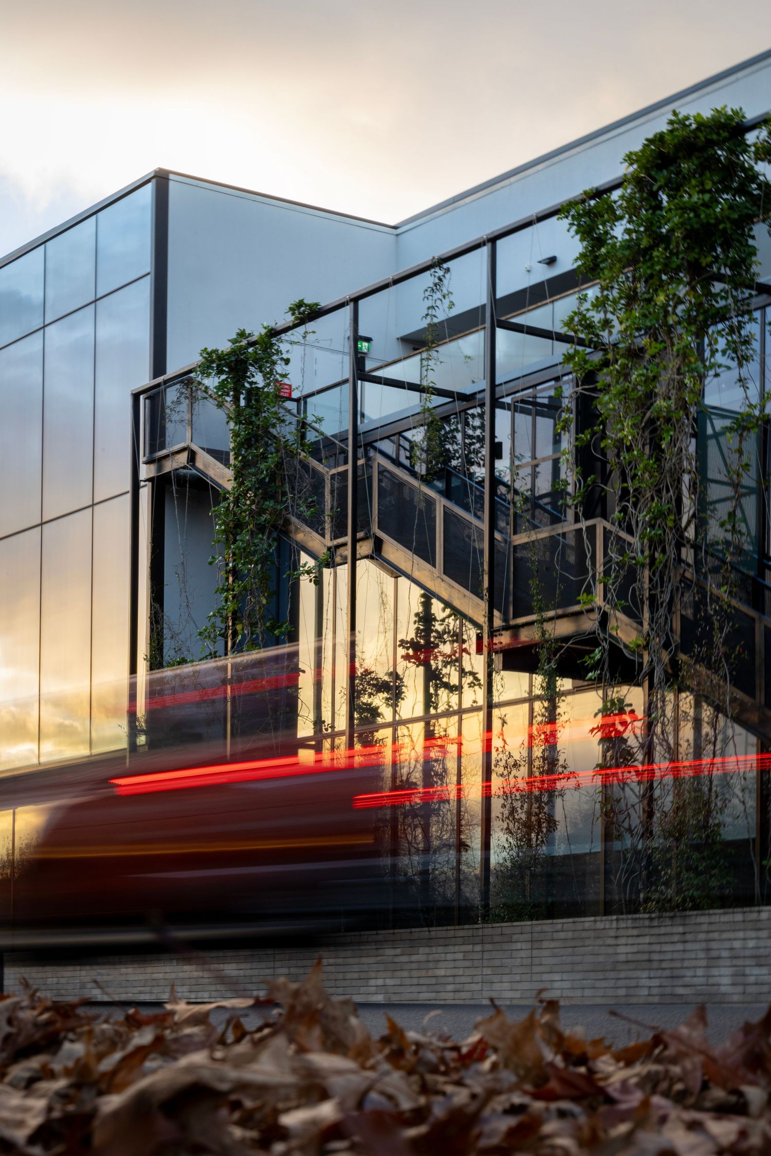 Modern glass building at dusk with light trails from a passing car.