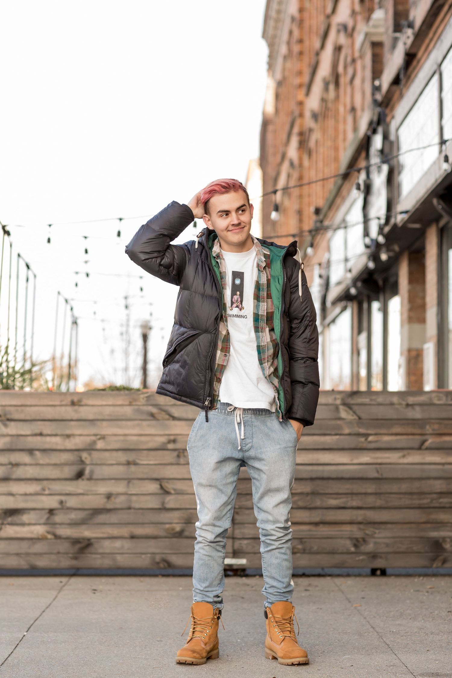 Stylish young man with pink hair in puffer vest and jeans posing on urban steps.
