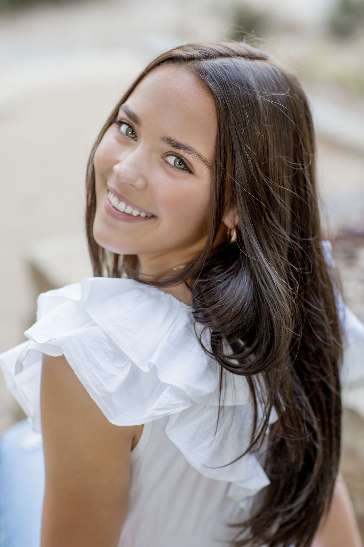Young brunette woman smiling in white ruffled top during an outdoor portrait session.