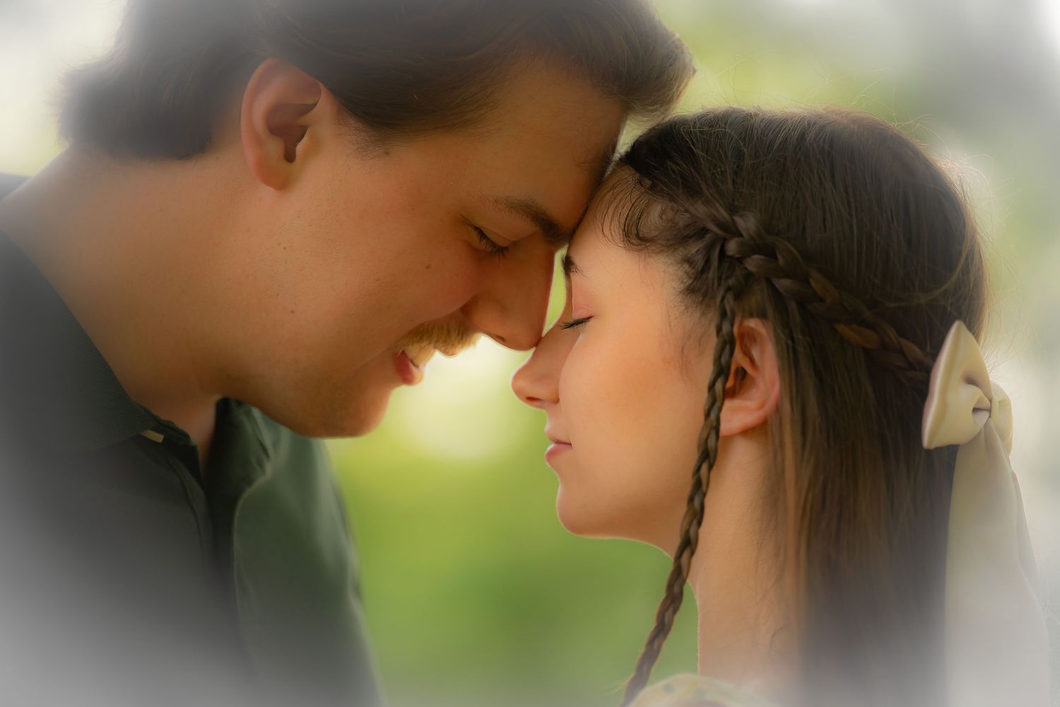 Romantic couple shares an intimate moment with foreheads touching against soft blurred background in their engagement portrait session.