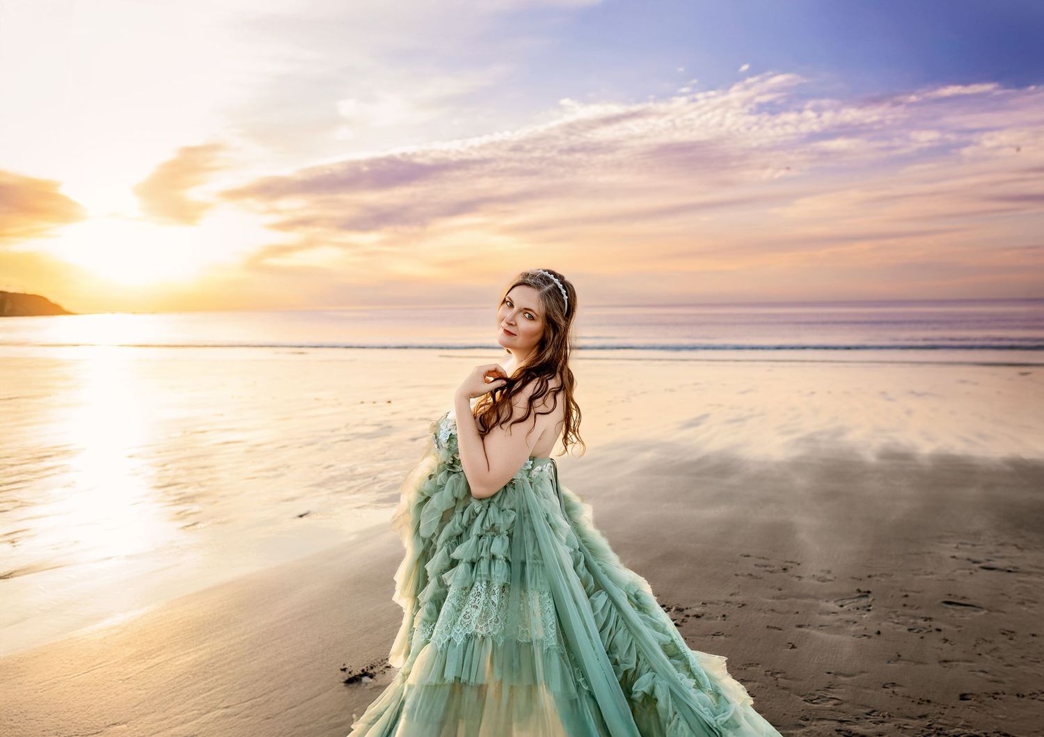 Woman in teal ruffled gown posing on beach at golden sunset.