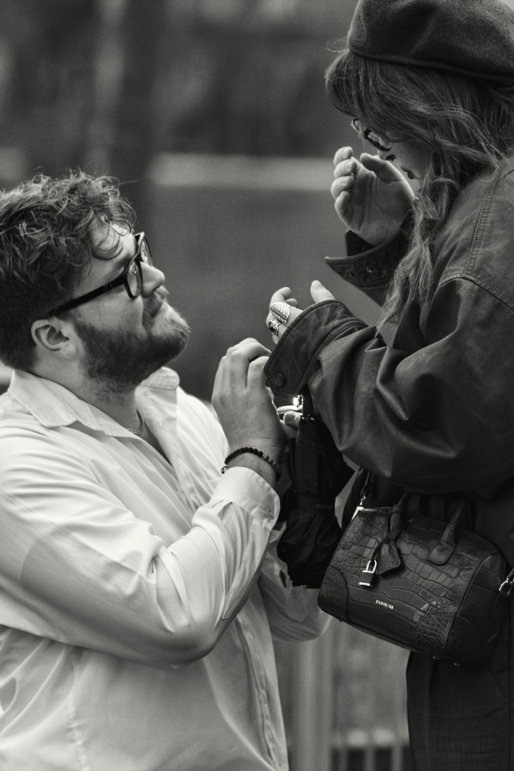 Black and white photo showing a romantic proposal scene outdoors with a person kneeling and offering a ring.