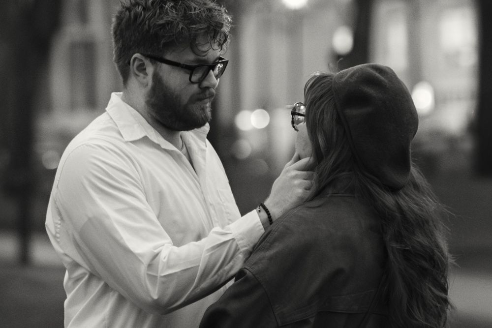 A tender moment captured in black and white as two people share an intimate conversation on a city street.