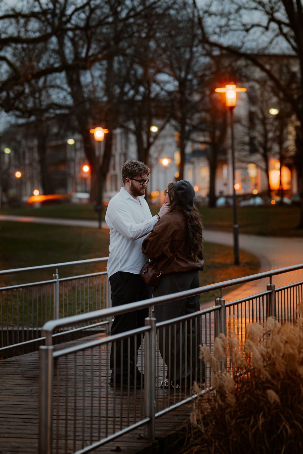 Silhouetted couple shares romantic moment on park pathway at dusk as glowing lampposts illuminate winter evening.
