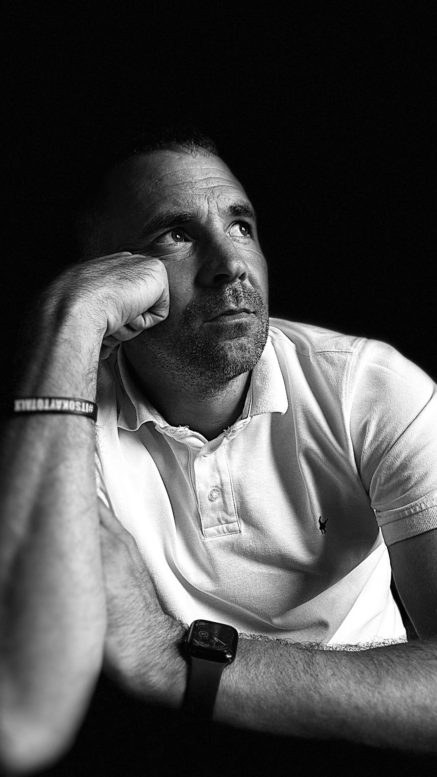 Dramatic black and white portrait of someone in polo shirt looking contemplatively upward.