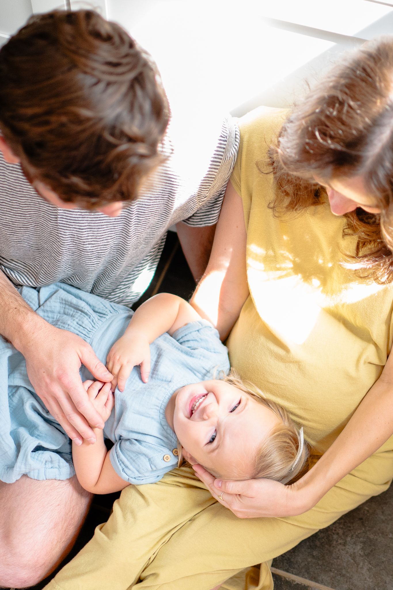 Little girl lays in mom and dad's laps during a studio mini session.