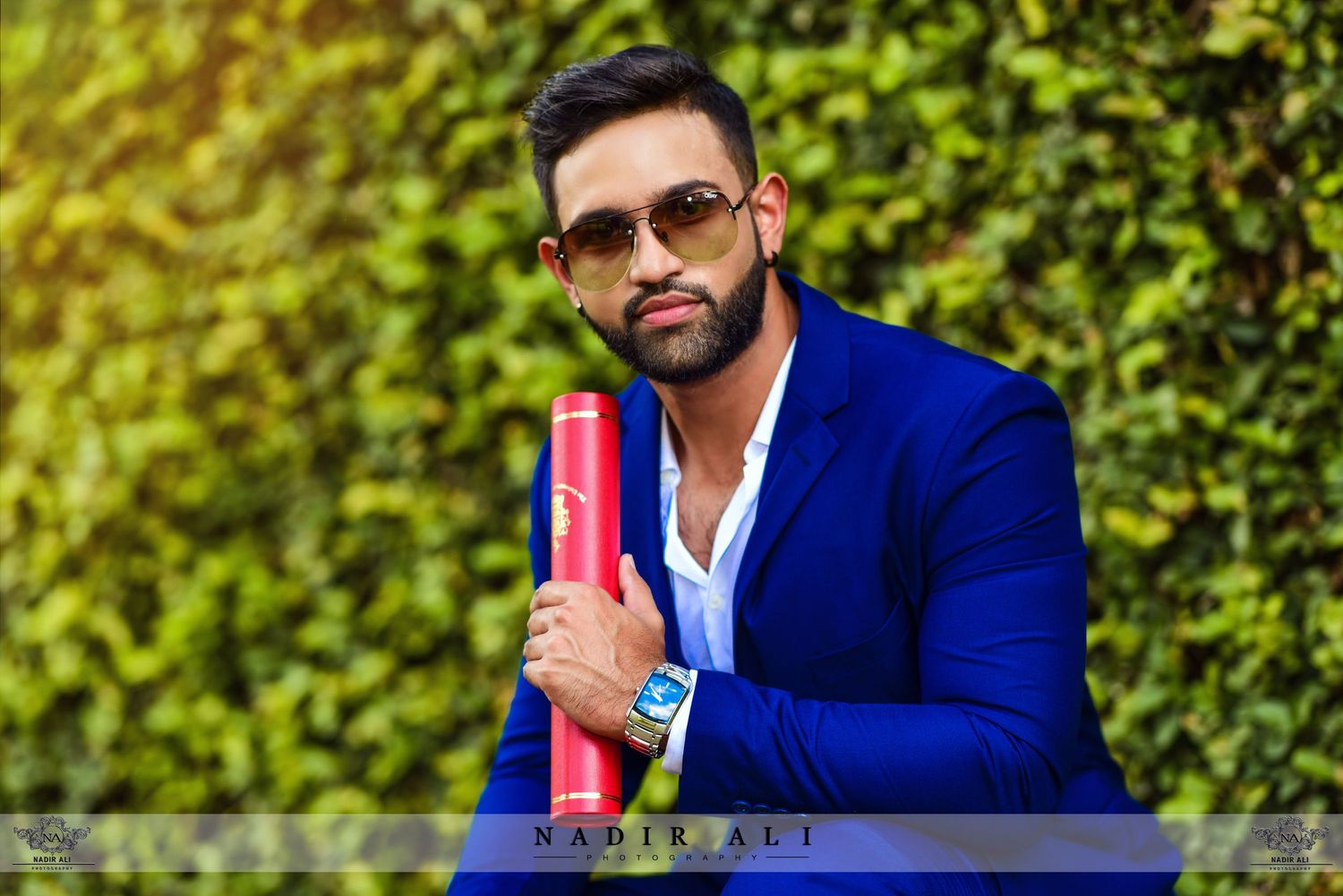 Professional in blue blazer holding a red cylinder against green foliage.