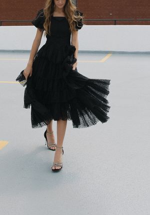 Elegant black tulle dress with flowing skirt and strappy heels photographed on concrete floor.