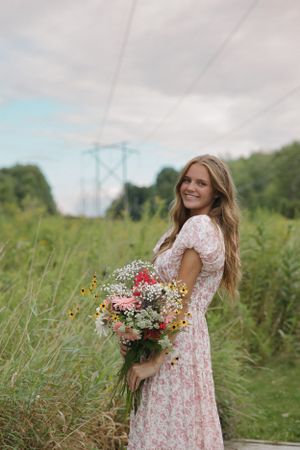Floral dress in meadow with wildflower bouquet and power lines in background.