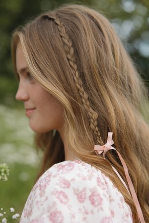 Romantic hairstyle with small braid and pink ribbon in long blonde hair.