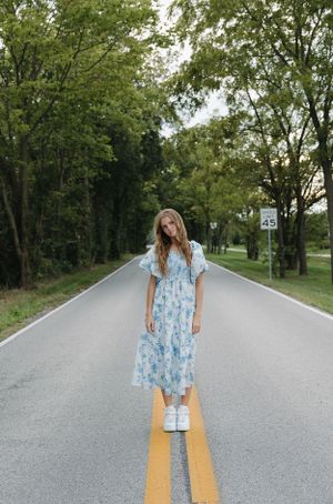 Standing on road center line wearing blue floral dress and white sneakers.