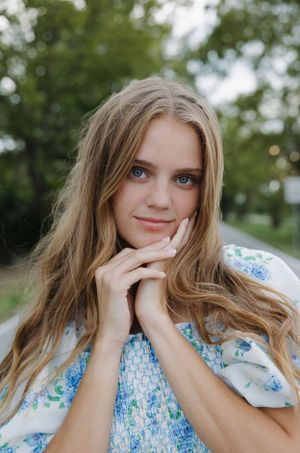 Close up portrait in blue floral dress against green summer foliage.