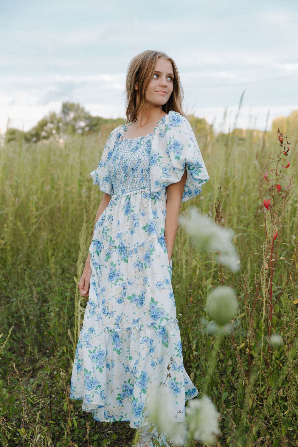 A flowy blue and white floral dress captured in a series of shots in a meadow of tall grass.