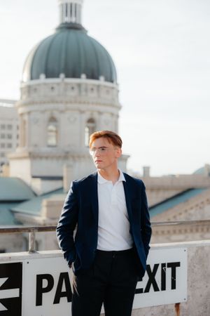 Person in business attire stands on rooftop with classic domed building architecture in background.
