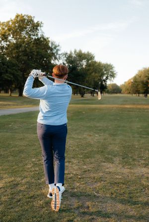Golfer in light blue sweater takes a swing on an autumn golf course.