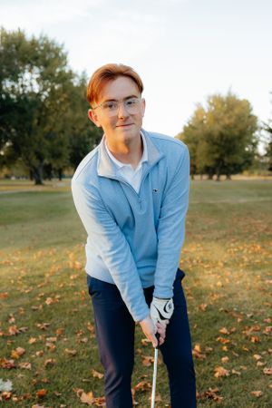 Golfer in casual attire practices putting stance on fall golf course.