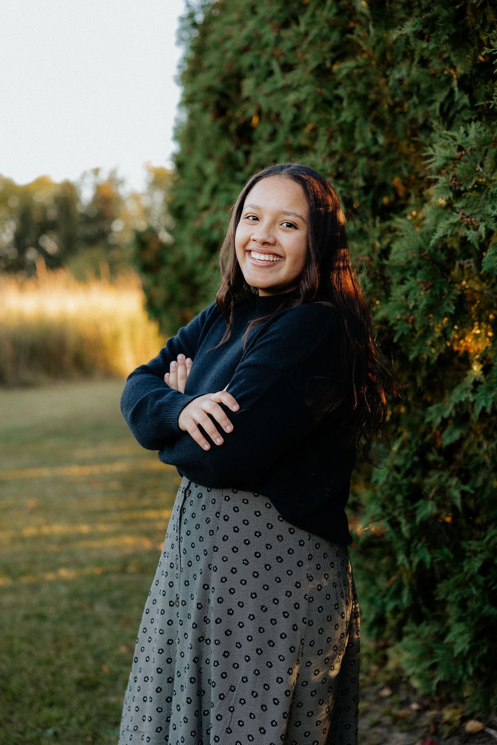 Outdoor portrait against evergreen hedge with autumn colors in background.