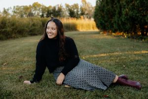 Relaxed outdoor portrait on grass wearing black sweater and patterned skirt.