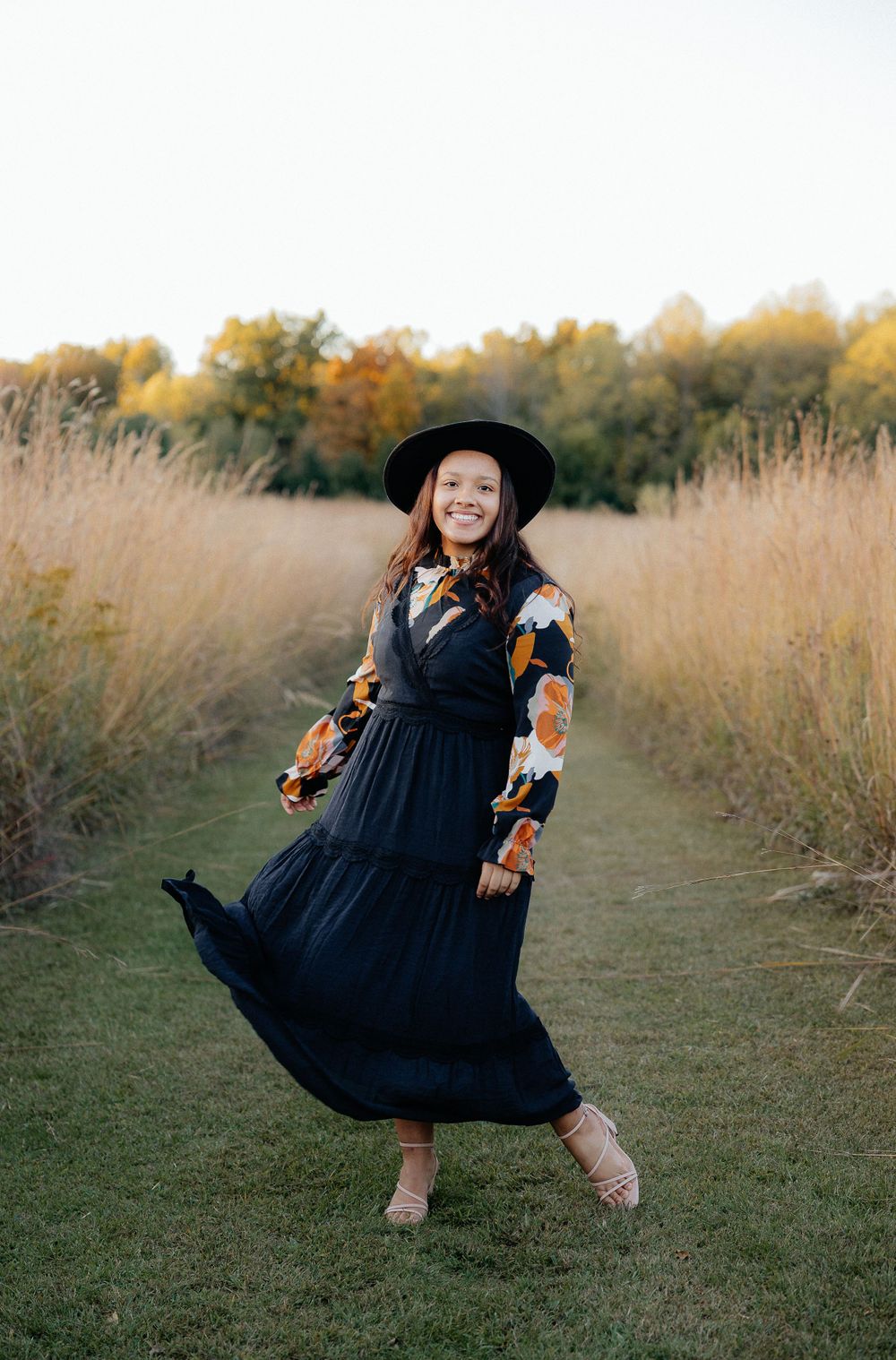 A person in a black dress twirls playfully in a golden autumn field at sunset.