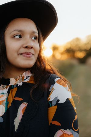 Close-up portrait showing a floral print dress and black hat against an autumn backdrop.