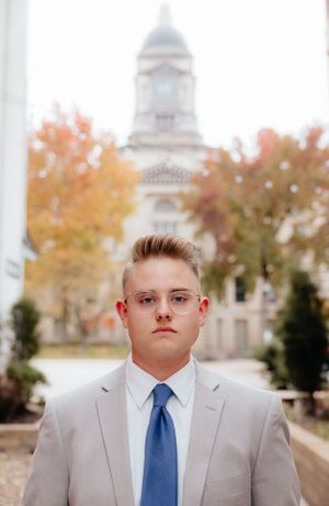 Professional portrait in front of historic building with autumn foliage and domed architecture in background.