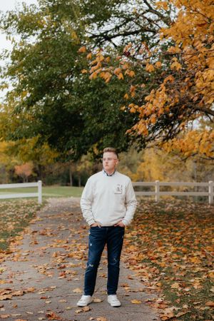 Autumn outdoor portrait with white fence, fallen leaves and golden trees.