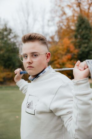 Golf-themed portrait outdoors with autumn scenery and golf club.