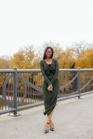A woman in a green dress poses elegantly on a bridge railing during autumn.