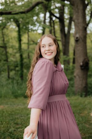 A mauve dress with puff sleeves photographed in a wooded outdoor setting.