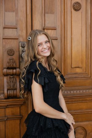 Woman in elegant black dress posing in front of ornate wooden doors.
