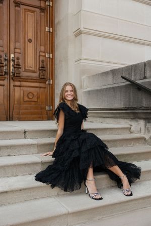 Woman in flowing black dress lounging gracefully on stone steps by wooden doors.