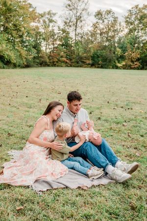 A family relaxes together on a blanket in a grassy field during an autumn afternoon photo session.